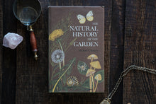 Book titled 'The Natural History of the Garden' by Michael Chinery on a wooden surface with natural items.