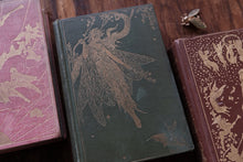Three vintage books with fairy illustrations on a wooden surface
