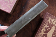 Vintage book with worn leather binding held by a hand on a wooden surface.