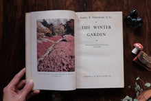 Open book titled 'The Winter Garden' on a wooden surface with decorative elements.