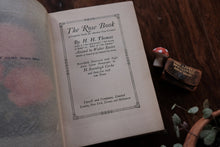 Vintage book titled 'The Rose Book' by H.H. Thomas on a wooden surface with decorative elements.
