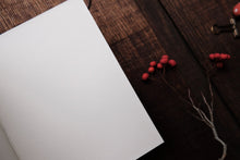 White notebook on a wooden surface with red berries and a key.