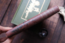 Brown leather-bound book with floral designs on a wooden surface