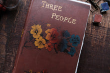 Book titled 'Three People' with floral design on a wooden surface
