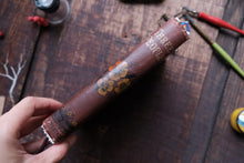 Hand holding a rolled-up scroll with decorative cover on a wooden surface