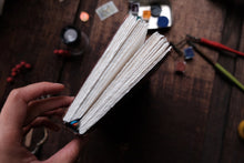 Hand holding a small notebook with stationery items on a wooden surface