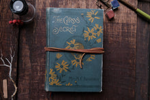 Vintage book titled 'The Gipsy's Secret' with floral design on a wooden surface.