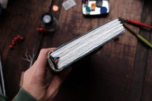 Hand holding a small notebook on a wooden surface with various items.