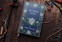 Book titled 'Janet Darney's Story' by Sarah Dowdney on a wooden surface with decorative items.