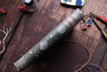 Roll of green paper with floral design on a wooden surface with stationery items.