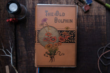 Vintage book titled 'The Old Dolphin' with floral design on a wooden surface.