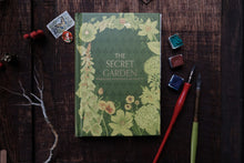 Book titled 'The Secret Garden' with floral design on a wooden surface with art supplies.