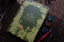 Book titled 'The Secret Garden' by Frances Hodgson Burnett on a wooden surface with writing utensils.