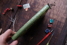Green book titled 'The Secret Garden' held by a hand on a wooden surface with art supplies.