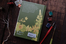 Green notebook with floral design on a wooden surface with art supplies