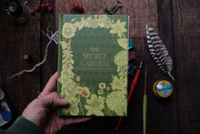 Hand holding a book titled 'The Secret Garden' with floral design on a wooden surface.