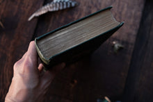 Hand holding an old book on a wooden surface with feathers