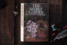 Book titled 'The Secret Garden' by Frances Hodgson Burnett on a wooden surface with decorative items.