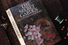 Book titled 'The Secret Garden' by Frances Hodgson Burnett on a wooden surface with decorative elements.