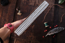 Hand holding a notebook with a wooden surface and sewing materials in the background