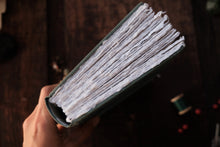 Hand holding a green notebook with textured pages against a dark background