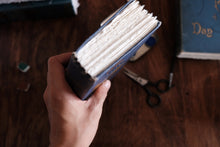 Hand holding a blue book with white pages on a wooden surface.