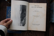 Open book titled 'The Sea and Its Wonders' by Cyril Hall on a wooden surface with other books.