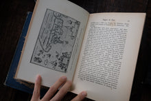 Open book with illustrations and text, held by a hand on a dark surface