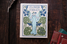 Book titled 'Flower Fables' by Louisa M. Alcott on a wooden surface with other books.
