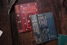 Two vintage books on a wooden surface with a feather and other books in the background.
