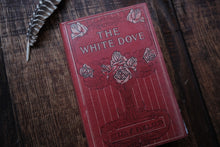 Red book titled 'The White Dove' on a wooden surface with a feather