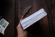 Hand holding a red-bound book with white pages on a wooden surface.