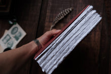 Hand holding a stack of white papers on a wooden surface with a feather and money in the background.