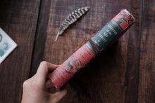 Vintage book with decorative cover held by a hand on a wooden surface