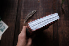Hand holding an open book with feather on a wooden surface