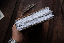 Hand holding a book with white pages on a wooden surface