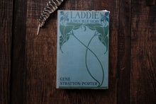 Vintage book titled 'Laddie: A True Blue Story' by Gene Stratton-Porter on a wooden surface with a feather.