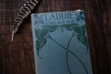 Book titled 'Laddie A True Blue Story' with a feather on a wooden surface