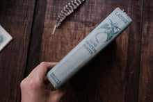 Hand holding a cylindrical product labeled 'Laddie' on a wooden surface with a feather and paper in the background.