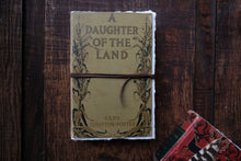 Book titled 'A Daughter of the Land' by Gene Stratton-Porter on a wooden surface