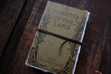 Book titled 'A Daughter of the Land' by Gene Stratton-Porter on a wooden surface
