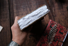 Hand holding an open book with white pages on a wooden surface