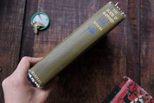 Hand holding a green book titled 'The House of Happiness' on a wooden surface.