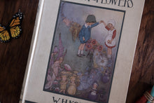 A vintage children's book titled 'Whispering Flowers' lying on a dark wooden surface, next to a small orange and black butterfly decoration. The book cover features an illustration of two children in a flower-filled scene.