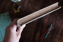A hand holding the edge of a thick, blank book with blank pages, set against a dark wooden background with soft-focus props.