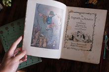 An open vintage book showing illustrated pages, held by a hand over a dark wooden surface, with another copy of the book partially visible on the left.