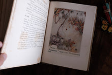 An open vintage book with printed text on the left page and a small illustrated page on the right, photographed on a dark wooden surface with a hand holding the left page.