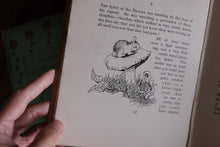 A hand holding an open vintage book, showing a page with printed text and a black-and-white illustration of a rabbit on a mushroom.